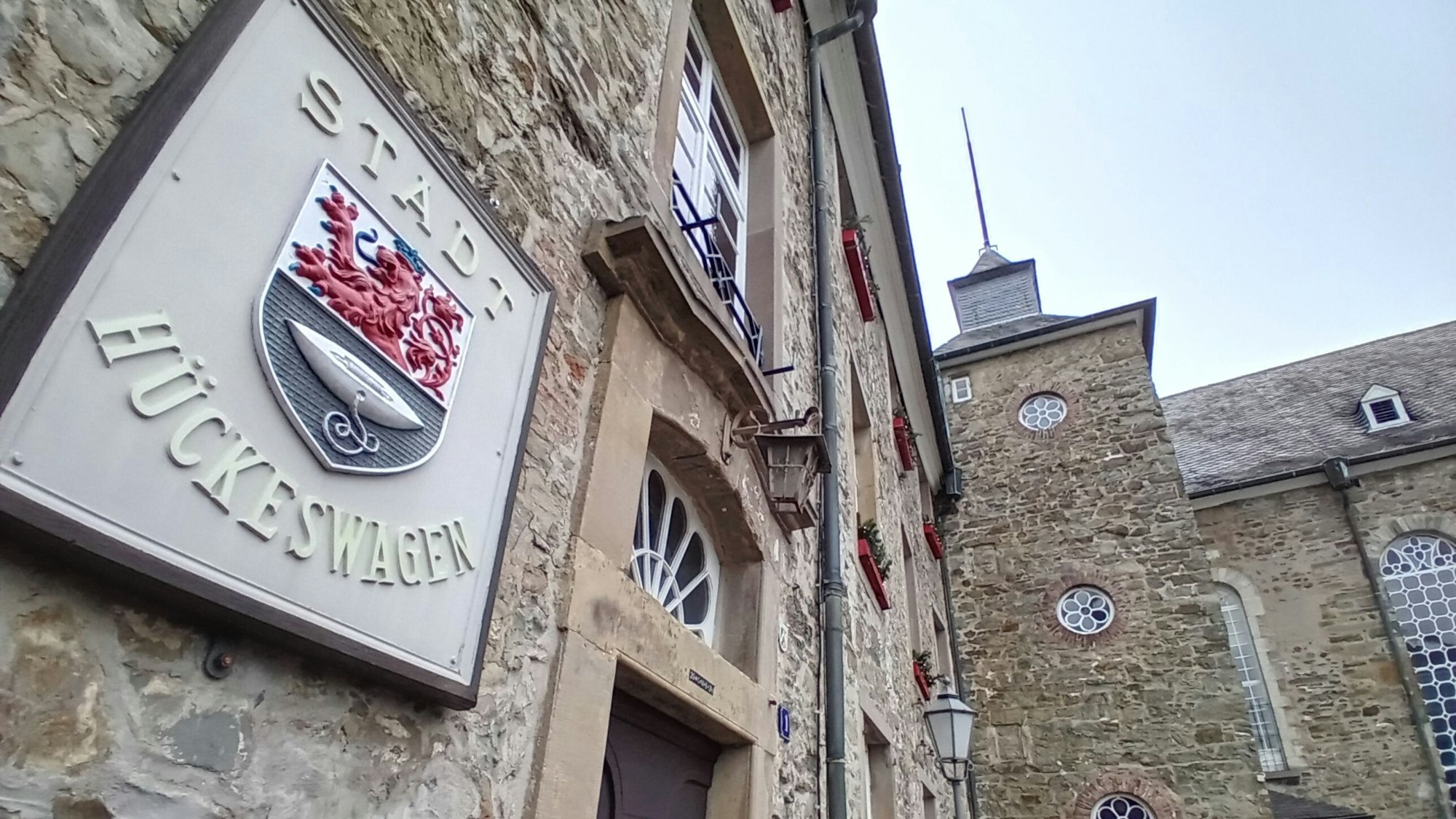 Vorn ein steinernes Wappen mit der Aufschrift Stadt Hückeswagen, im Hintergrund das Schloss.