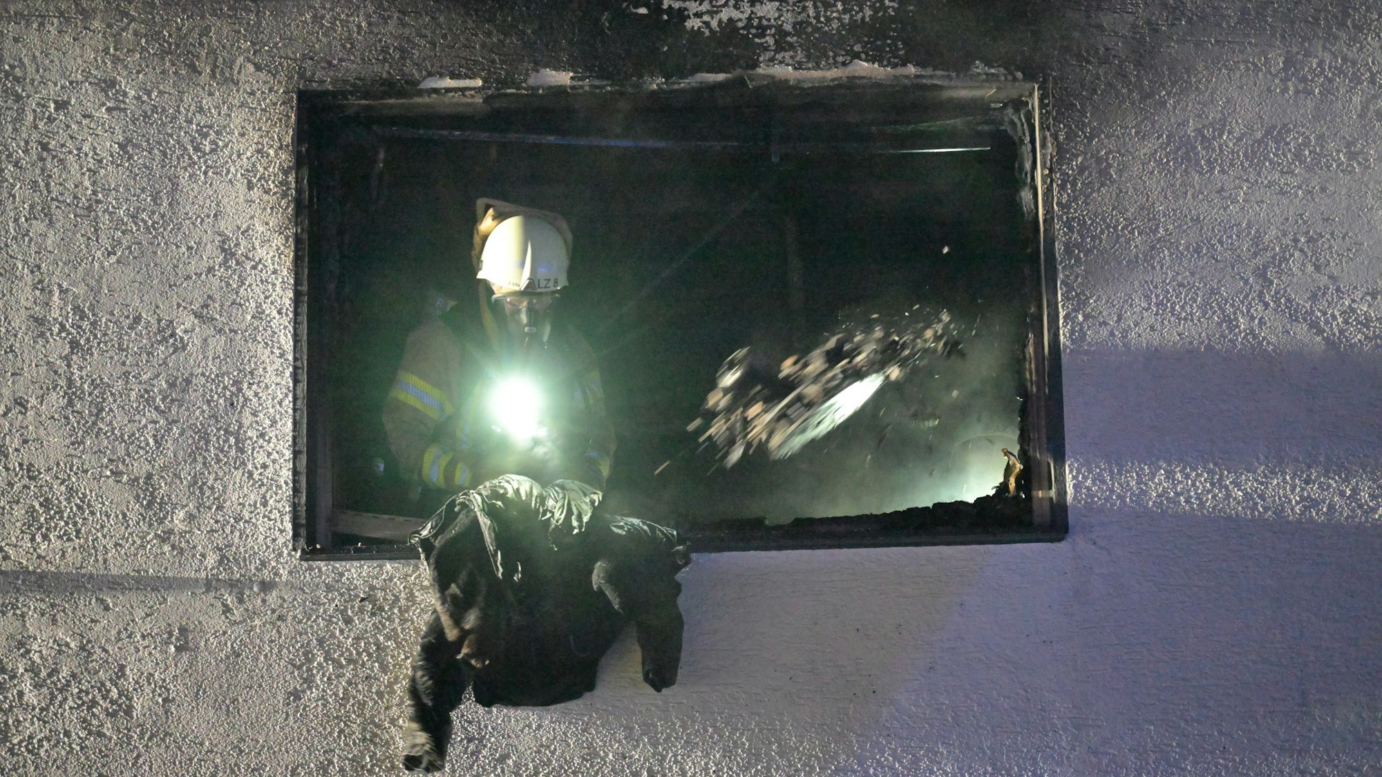 Ein Feuerwehrmann wirft eine Jacke aus dem Fenster einer Brandwohnung in Bergisch Glabach-Voislöhe.