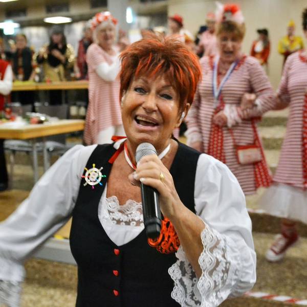 Marita Köllner singt und strahlt in die Kamera. Im Hintergrund schunkeln kostümierte Besucher.