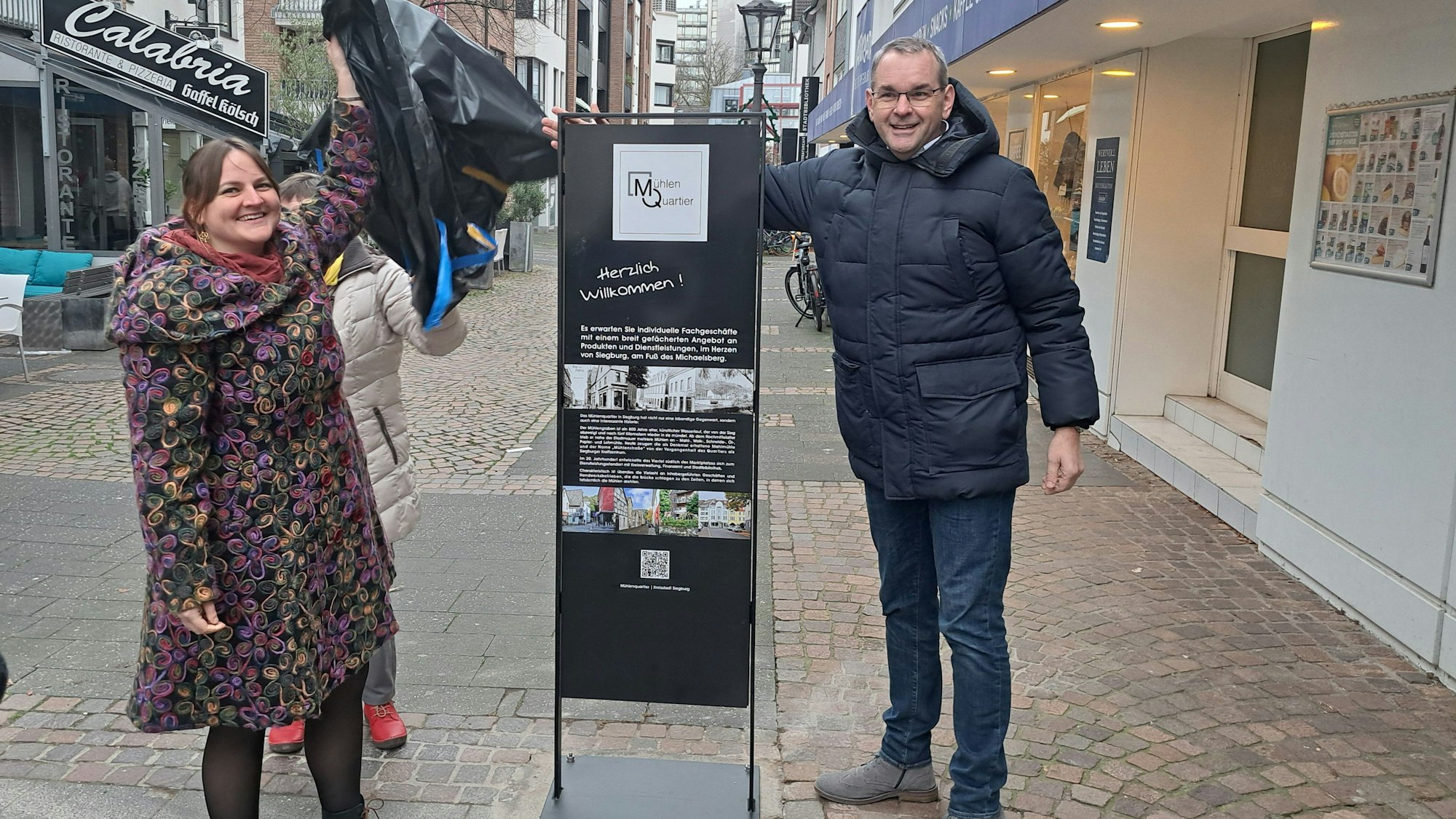 Eine neue Stele lädt jetzt in das Siegburger Mühlenquartier ein. Nadine Weißenfels von der Initiative Mühlenquartier und Bürgermeister Stefan Rosemann enthüllten das Schild.