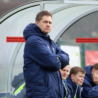 Trainer Kevin Greuel steht mit verschränkten Armen vor der Ersatzbank.