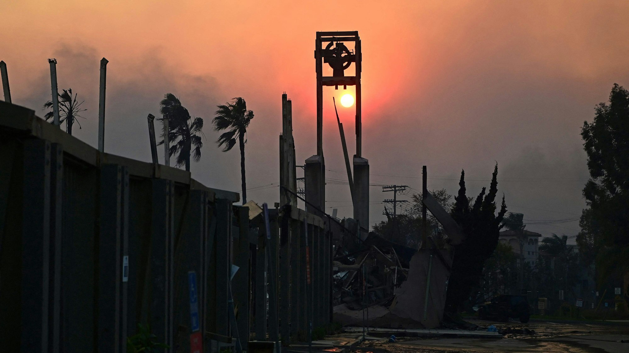 The sun is seen through smoke behind the ruins of the Pacific Palisades Presbyterian Church after the passage of the Palisades Fire in Pacific Palisades, California, on January 8, 2025. At least five people have been killed in wildfires rampaging around Los Angeles, officials said on January 8, with firefighters overwhelmed by the speed and ferocity of multiple blazes. (Photo by AGUSTIN PAULLIER / AFP)