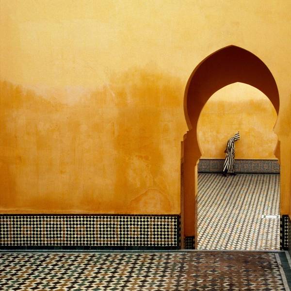 Die Aufnahme „MOROCCO. Meknes. Moulay Ismael Mausoleum (Muslim shrine). 1985“ zeigt den Blick durch ein Tor, im Hintergrund steht ein Mann mit einer gestreiften Kutte mit Kapuze.