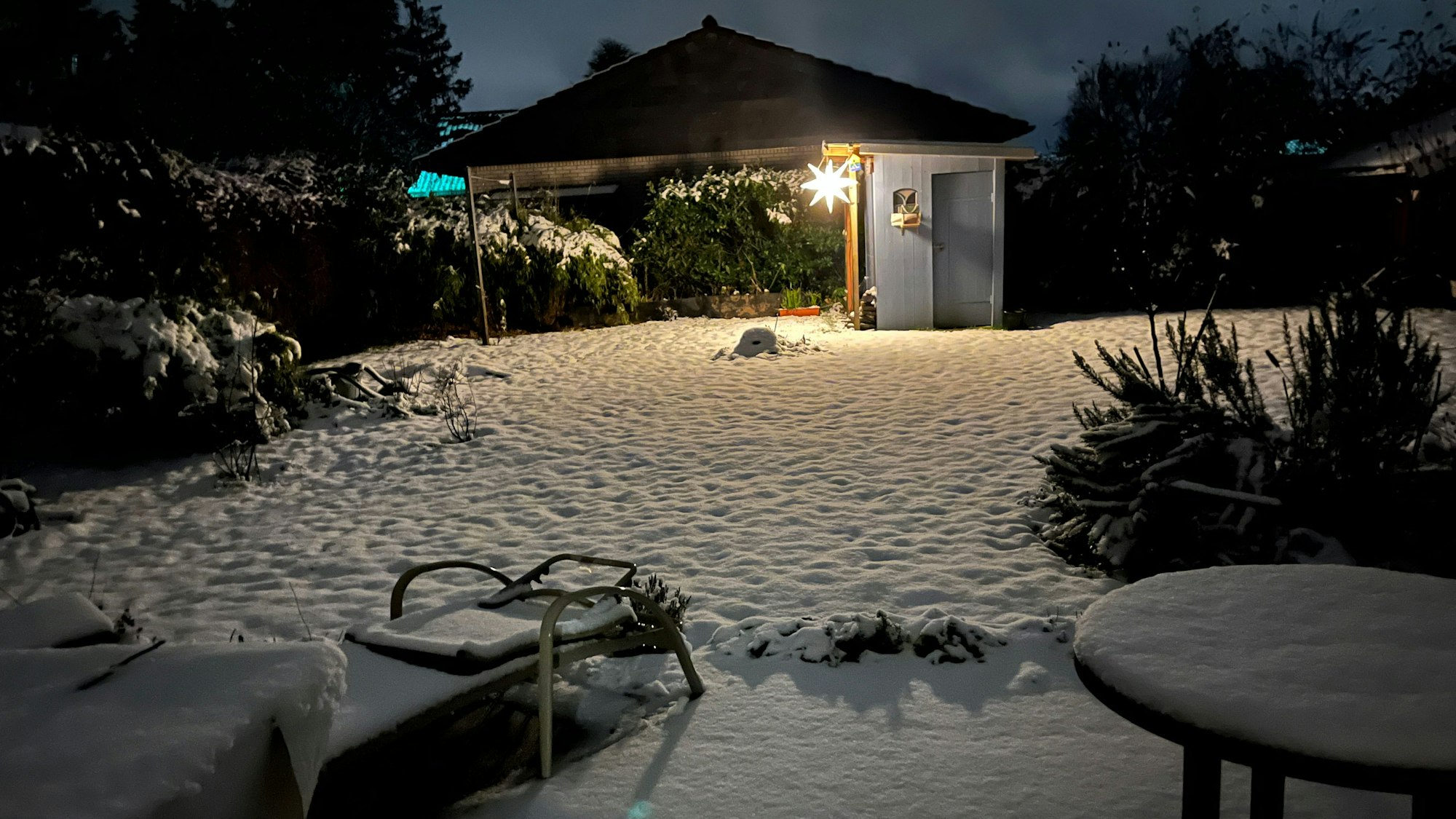 In einem Garten liegt eine geschlossene Schneedecke.