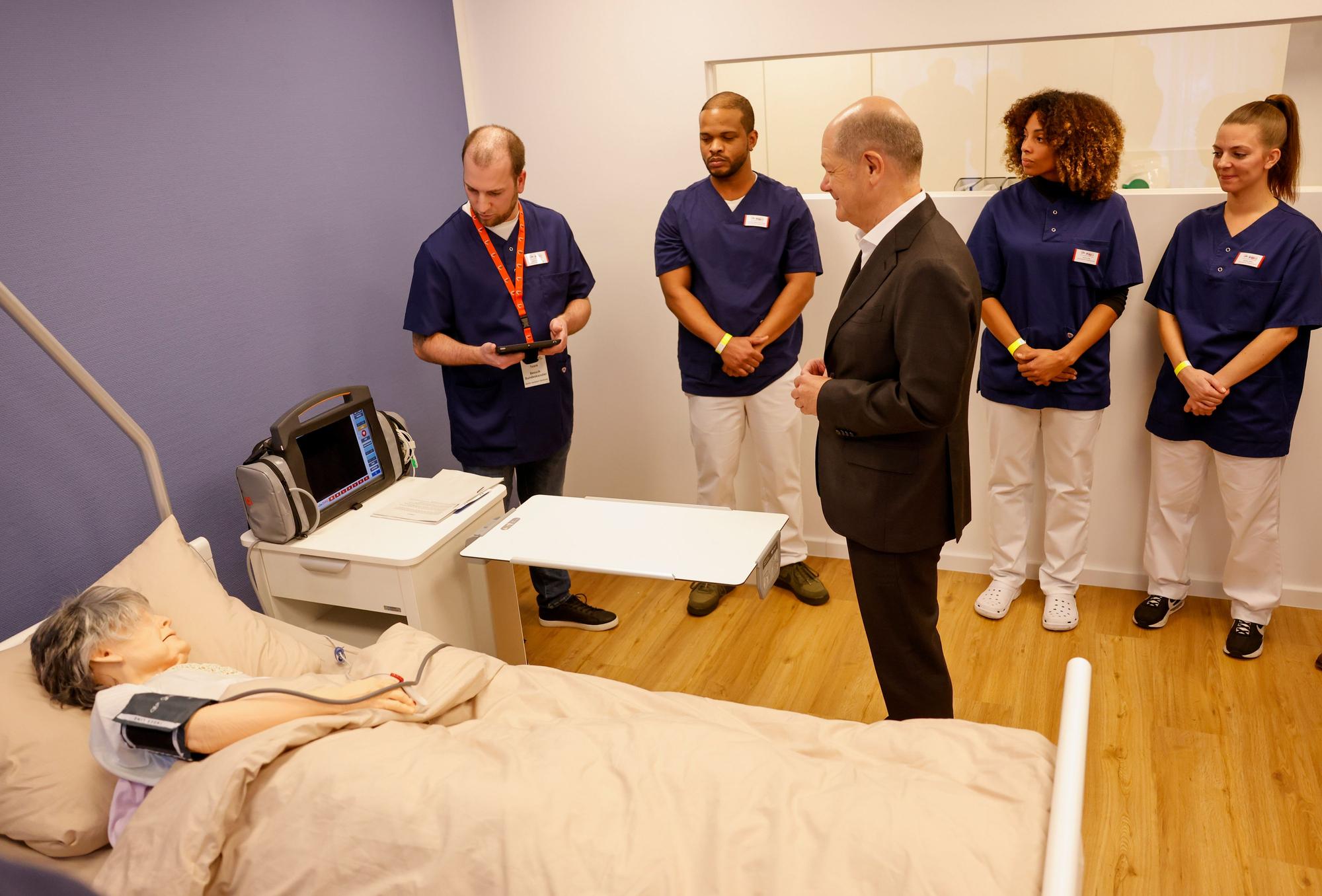 Auszubildende der Awo zeigen Bundeskanzler Olaf Scholz eine wirklichkeitsnahe Puppe, an der krankenpflegerische Tätigkeiten geübt werden können.
