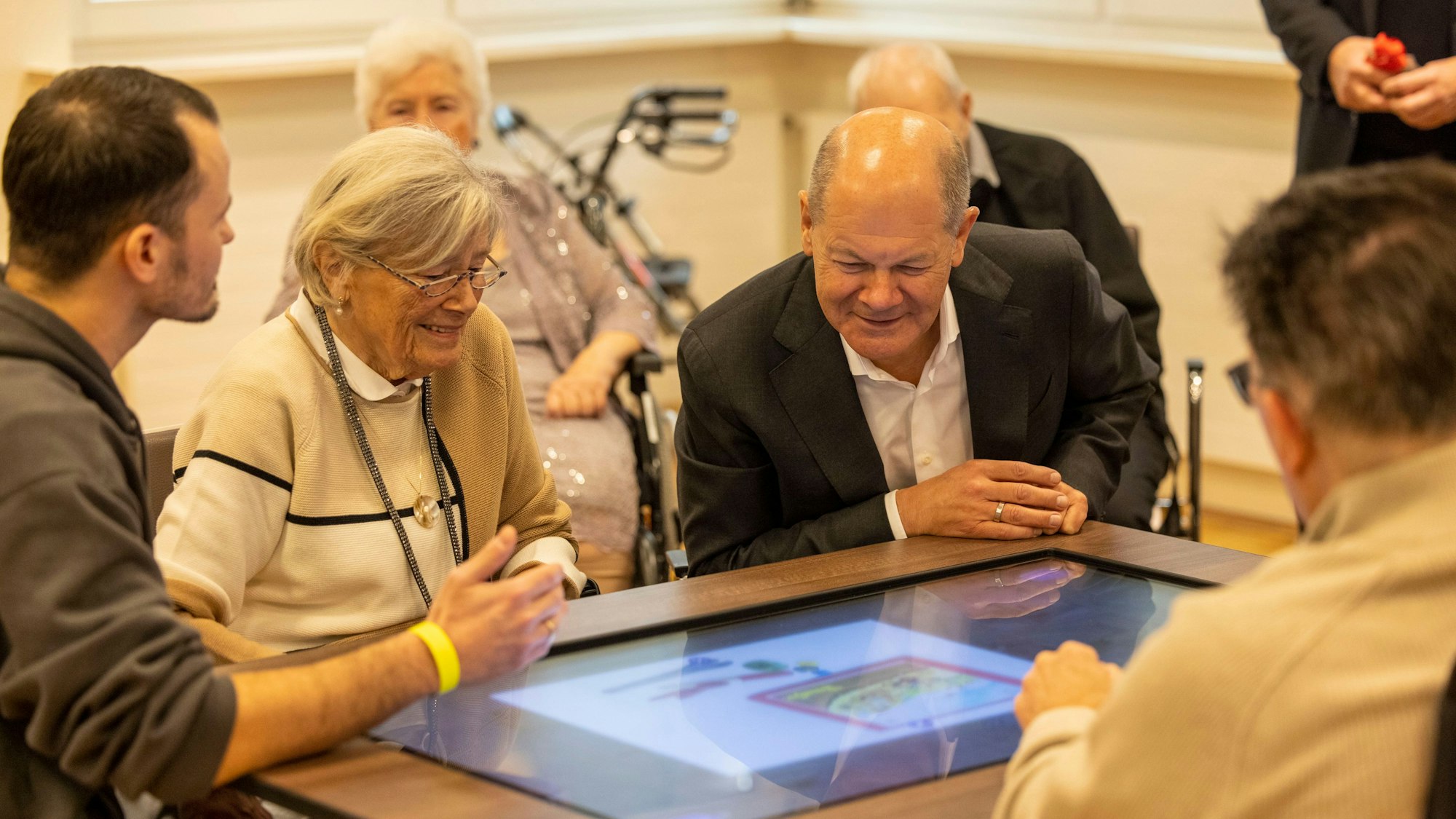Bundeskanzler Olaf Scholz schaut mit Bewohnern eines Seniorenzentrums auf einen digitalen Spieltisch.