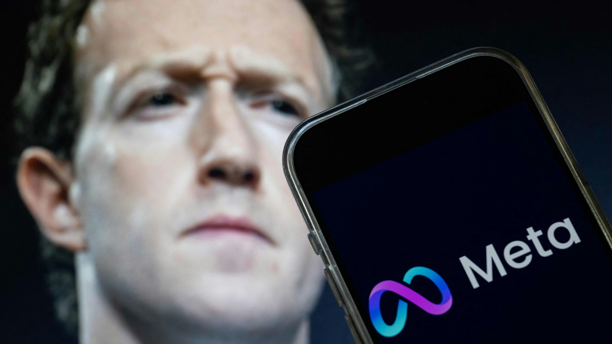 Konzernchef Mark Zuckerberg neben einem Smartphone, auf dessen Bildschirm das Logo von Meta zu sehen ist.