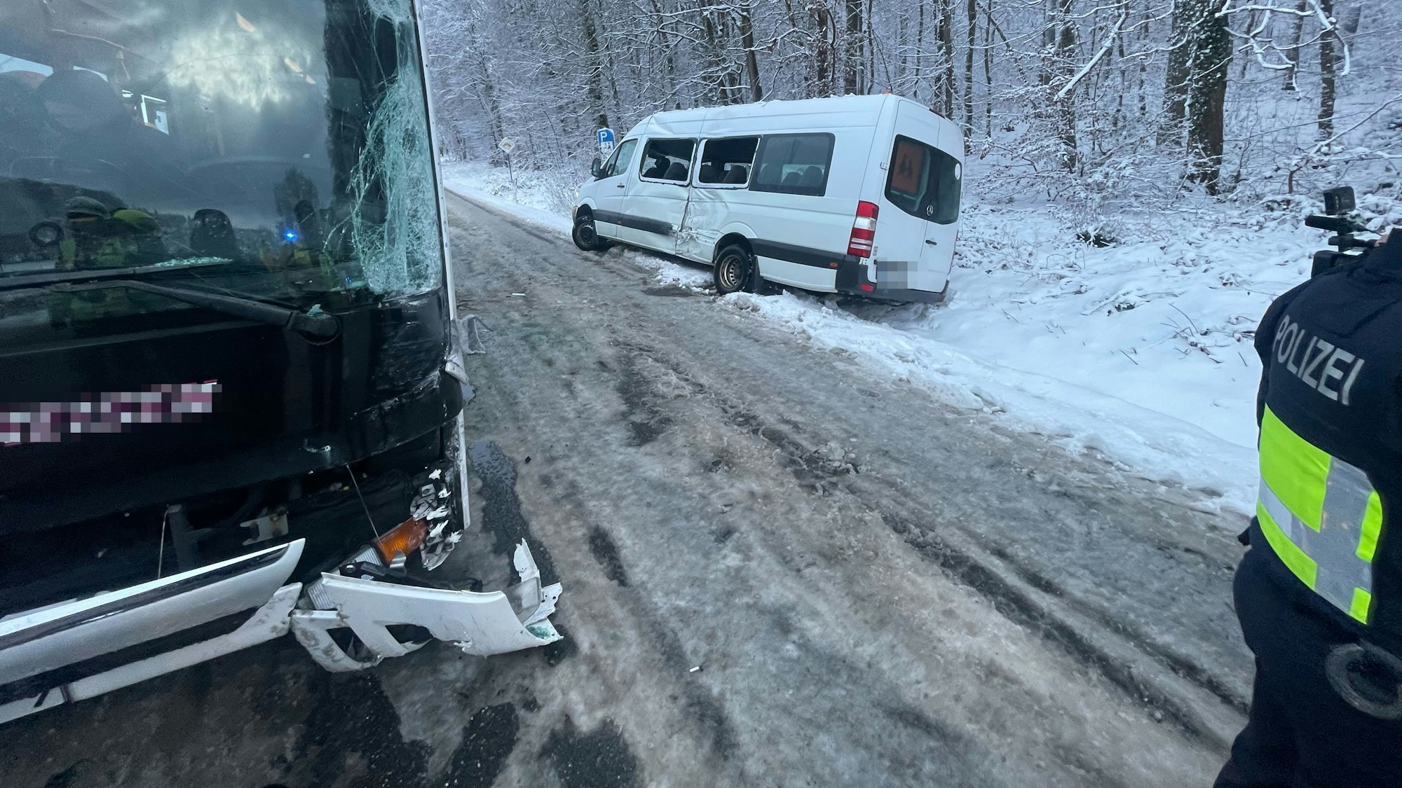 Nach einem Unfall auf einer mit Schnee und Eis bedeckten Straße ist ein beschädigter Kleinbus im Graben, ein Reisebus steht auf der Straße.