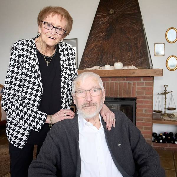 Marliese Hück steht hinter ihrem Mann Klaus, der im Wohnzimmer sitzt.