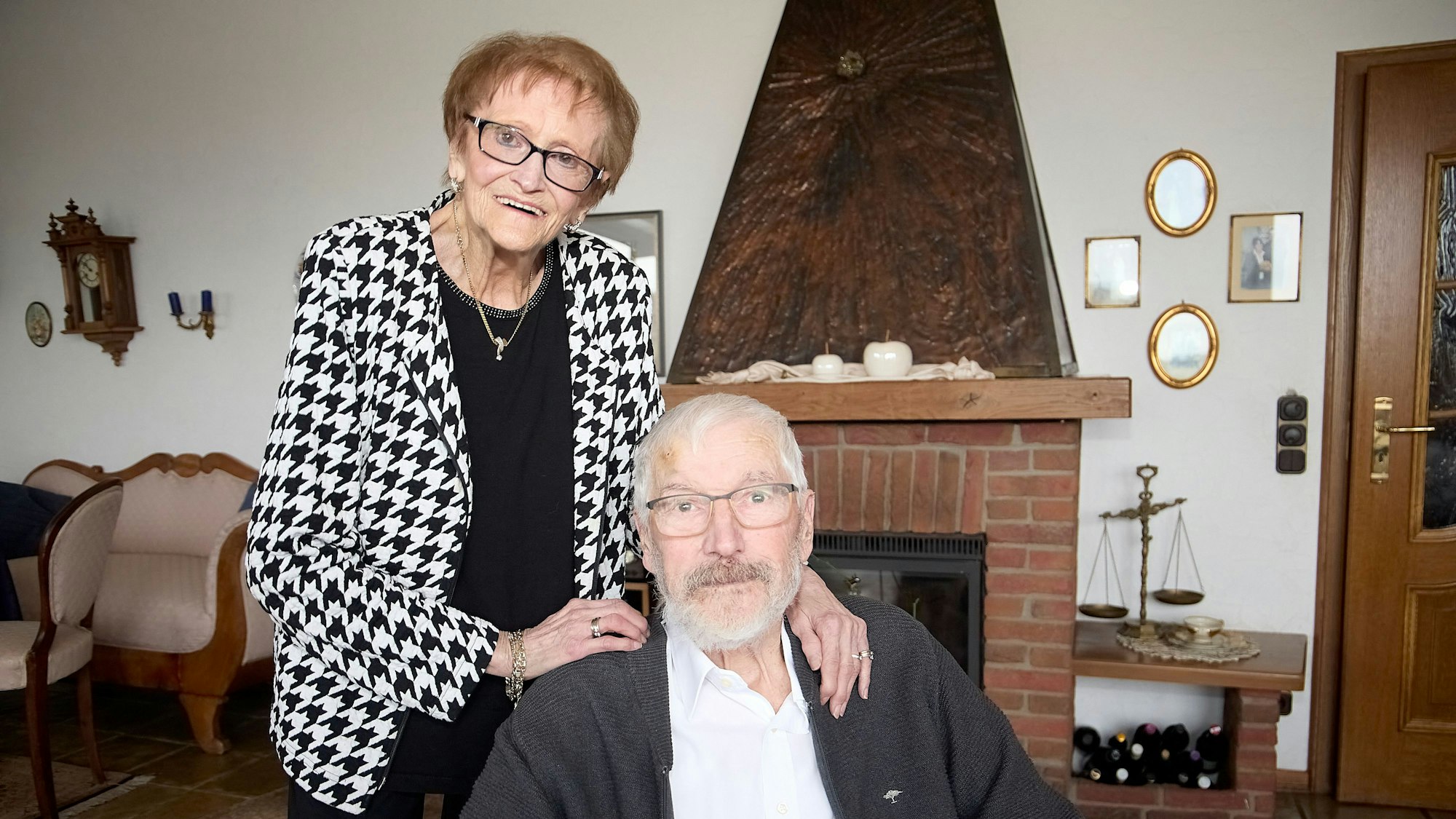 Marliese Hück steht hinter ihrem Mann Klaus, der im Wohnzimmer sitzt.
