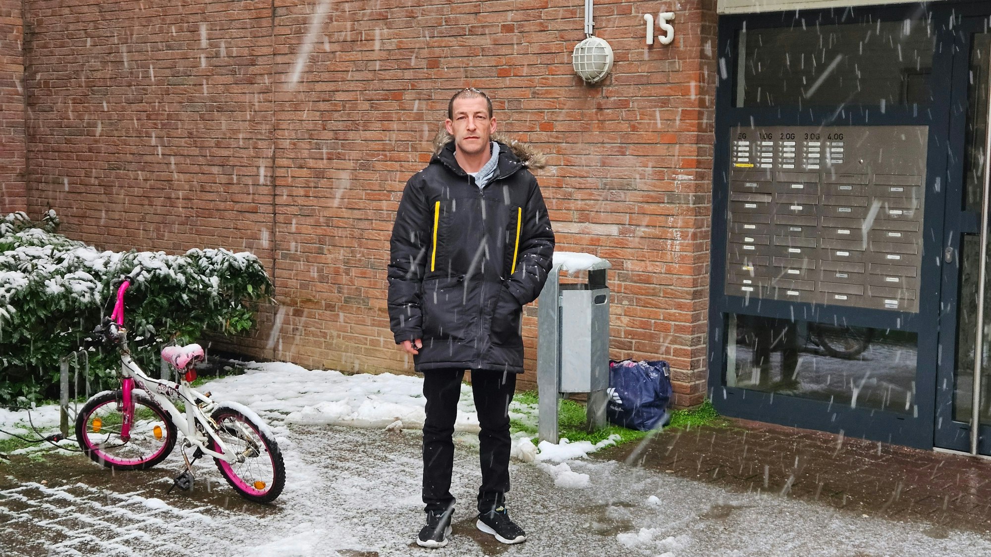 Ein Mann steht bei Schneefall vor einem Hauseingang.