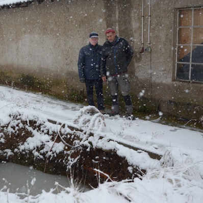 Zwei Männer stehen vor einer zur Hälfte mit Wasser gefüllten Grube.