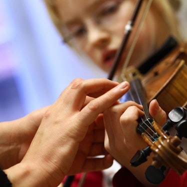 Das Foto zeigt die Hand einer Musikschülerin, die von einer Musiklehrerin beim Geigespiel korrigiert wird.