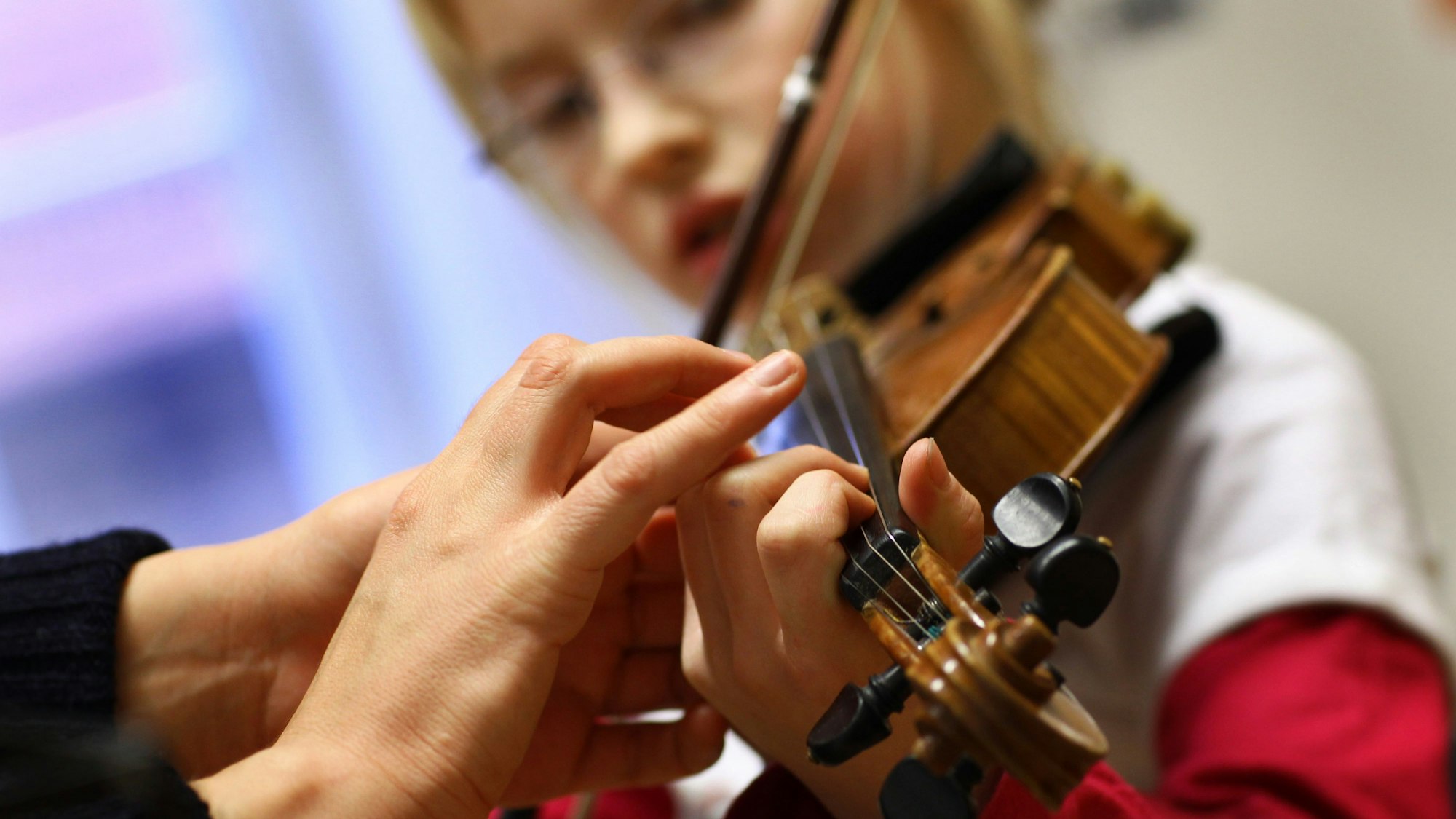 Das Foto zeigt die Hand einer Musikschülerin, die von einer Musiklehrerin beim Geigespiel korrigiert wird.