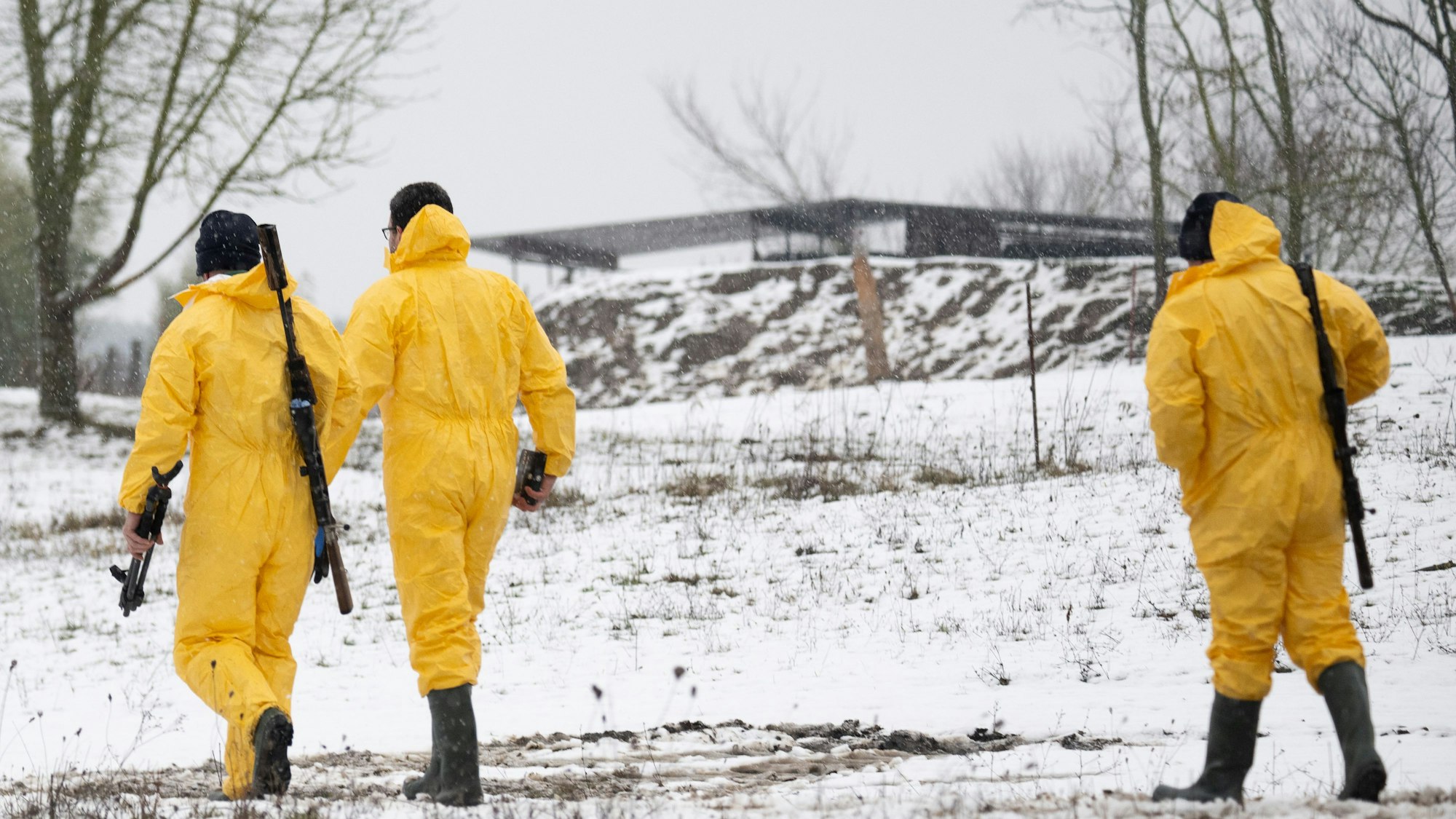Männer in Schutzkleidung und mit Gewehren gehen zu einem Stall. In dem Betrieb gibt es Fälle der Maul- und Klauenseuche in Brandenburg.