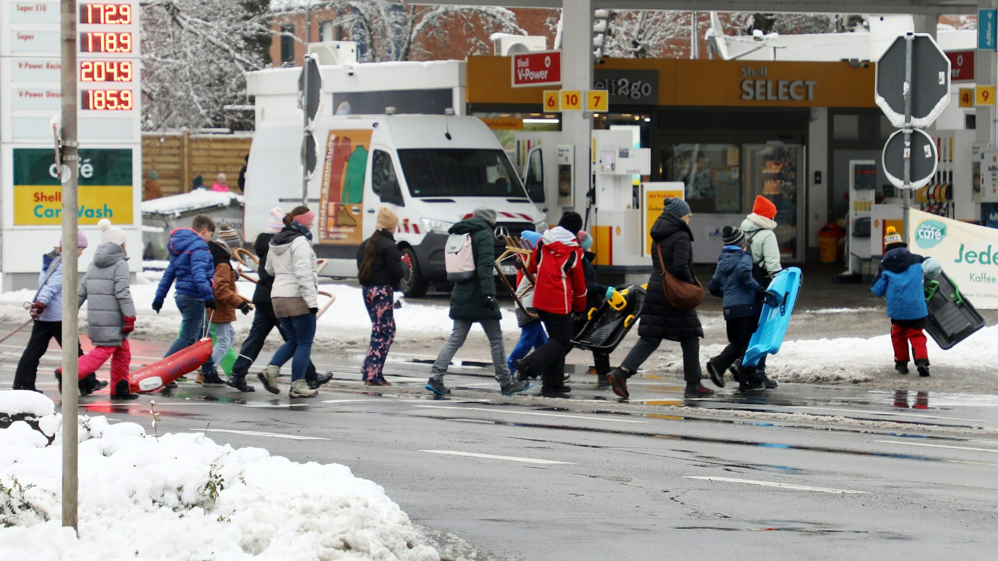 Kinder gehen mit Rodel und Schlitten über eine Straße in Bergisch Gladbach-Moitzfeld.