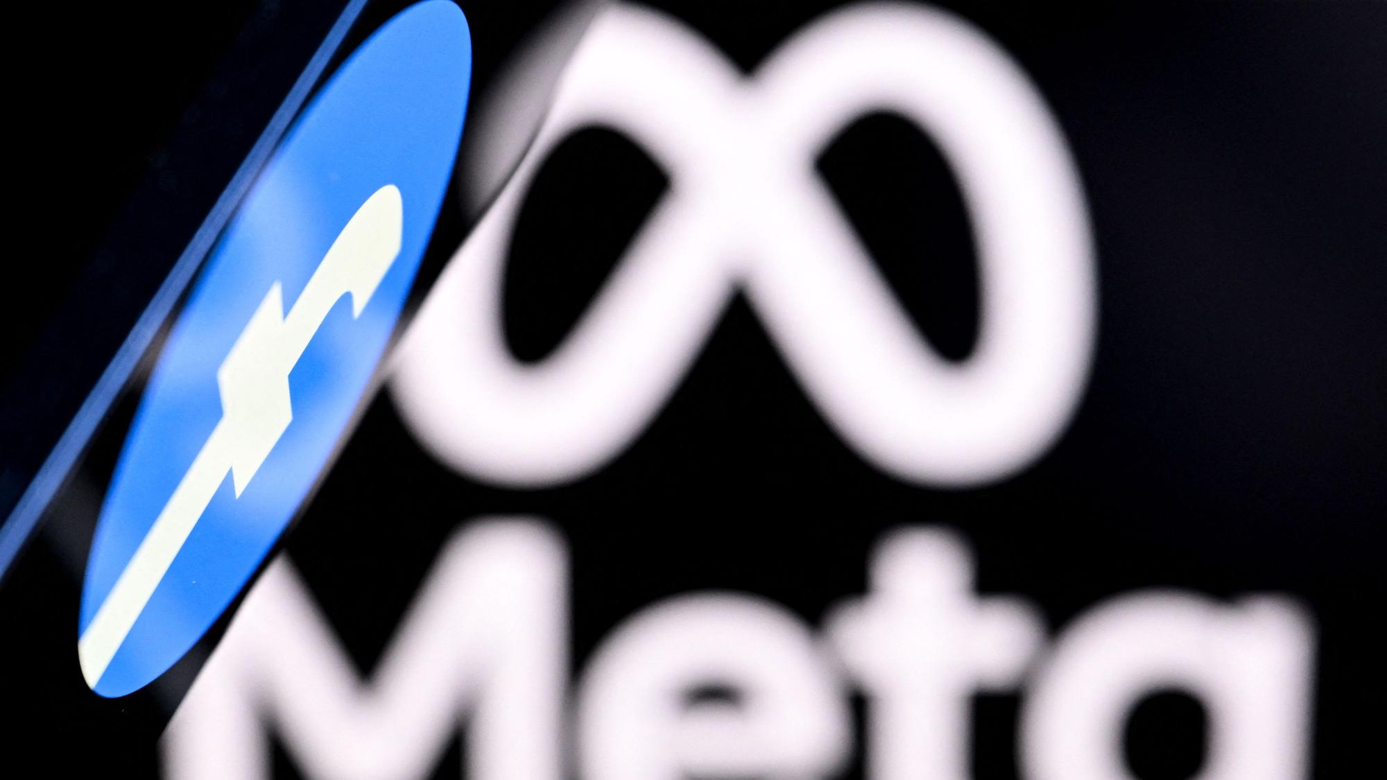 Ein Smartphone mit einem Facebook-Logo auf dem Bildschirm wird vor einen unscharfen Hintergrund mit Meta-Logo gehalten.