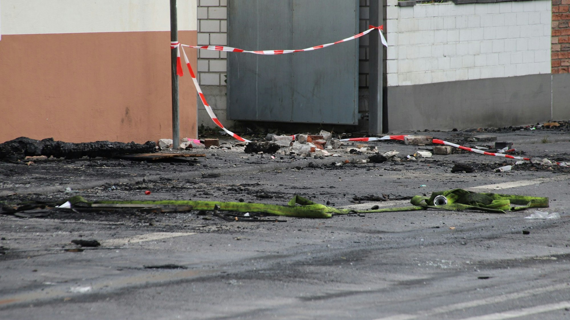 Ein Schlauch liegt vor einem ausgebrannten Gebäude auf der Straße.