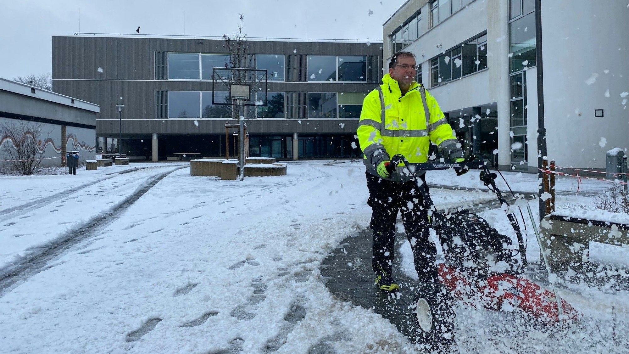 Zu sehen ist der Schulhof, der von Schnee befreit wird und im Hintergrund der Schulneubau.