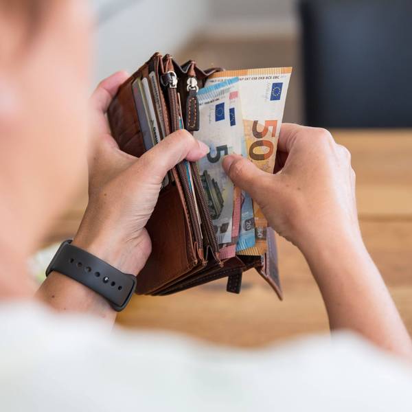 Eine Person hält eine Geldbörse mit Bargeld in den Händen. Die Geldscheine haben die Währung Euro und sind von unterschiedlichem Geldwert.