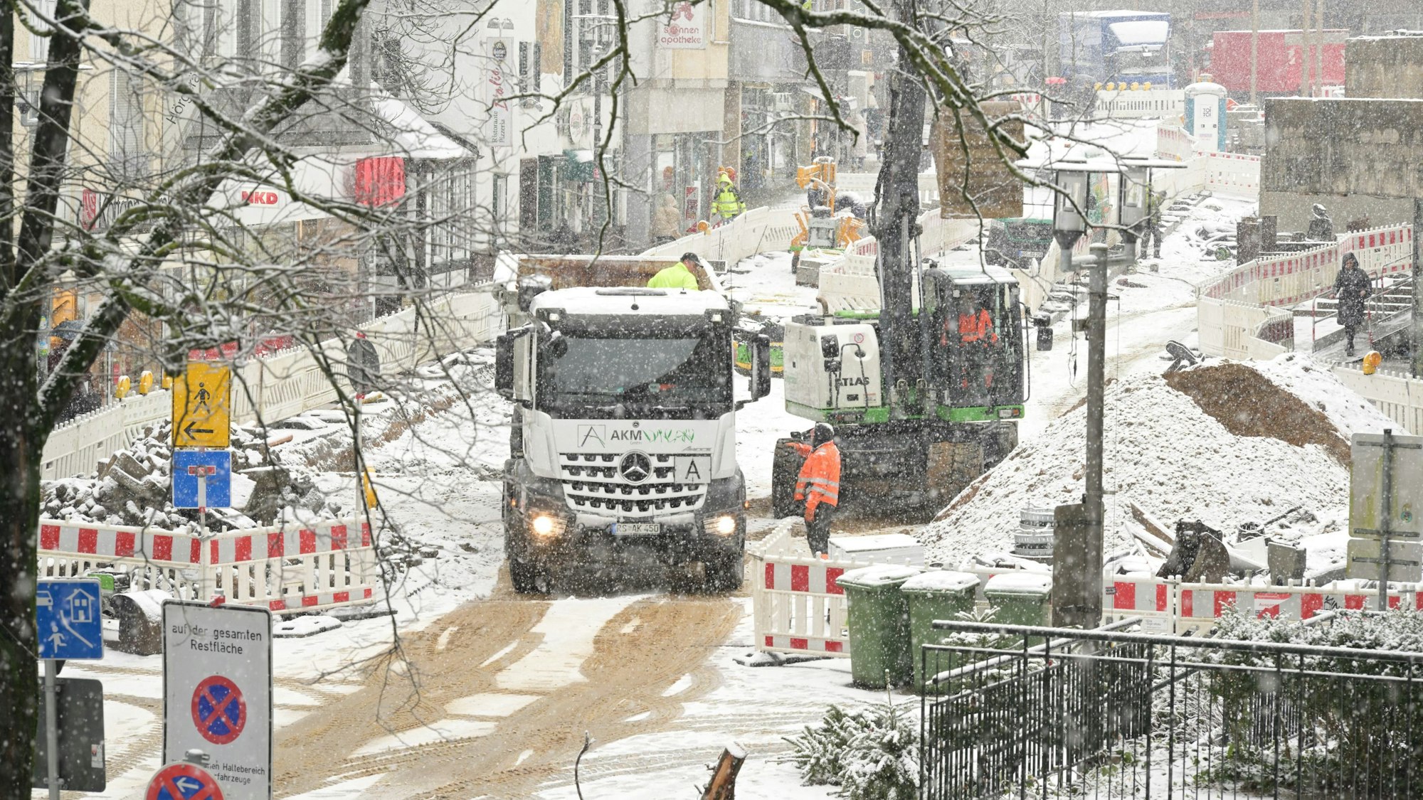 Hinter der Absperrung sind Baufahrzeuge und Bauarbeiter in roten Westen zu sehen.