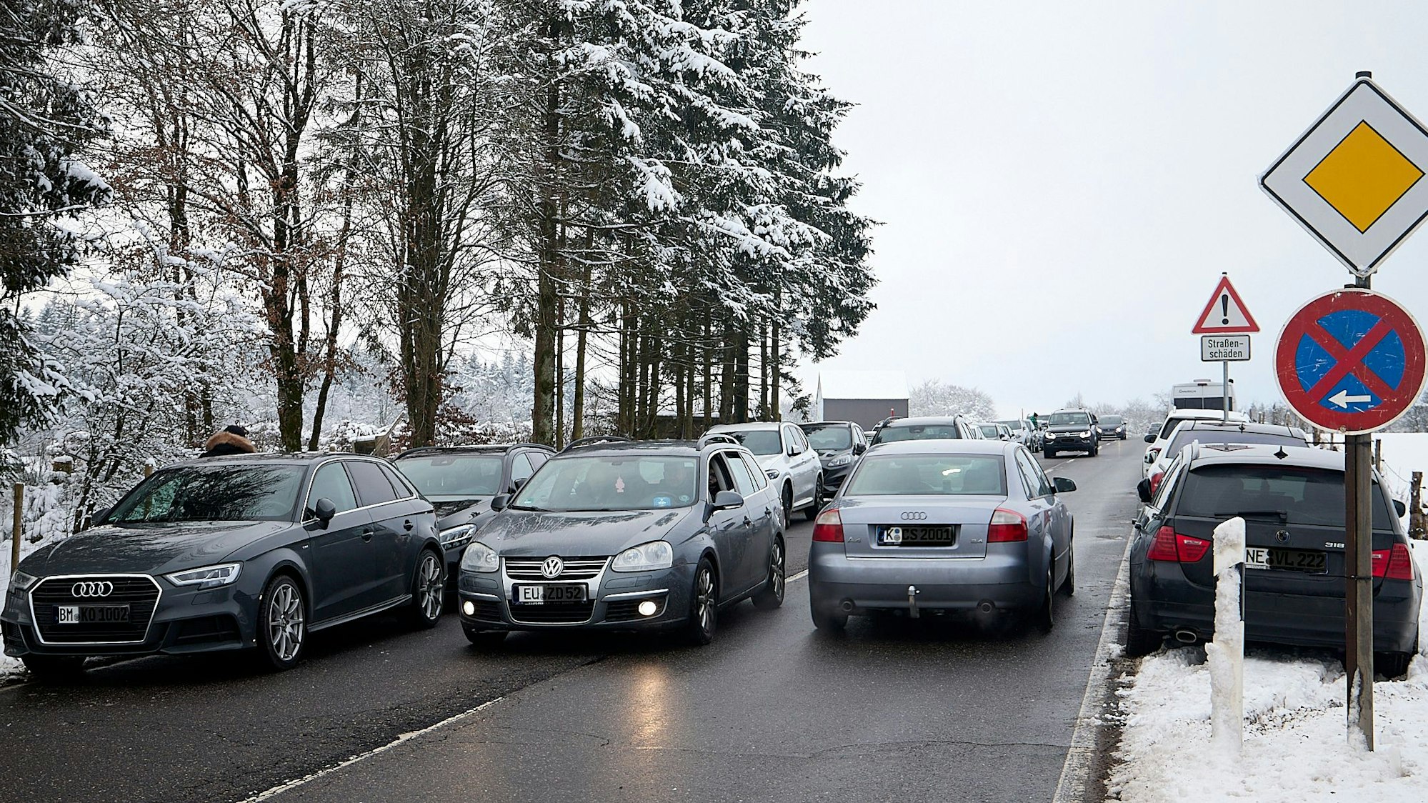 Zahlreiche Autos parken rechts und links einer Straße im Schnee.