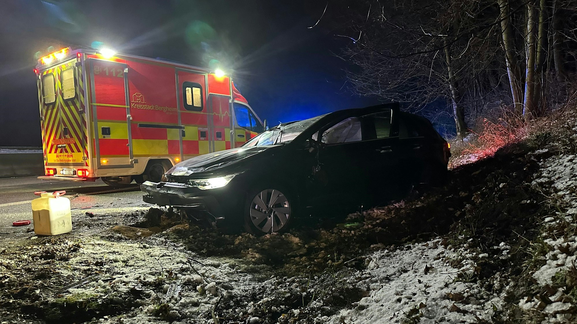 Ein zerstörtes Auto steht in einem Graben, dahinter steht ein Rettungswagen.