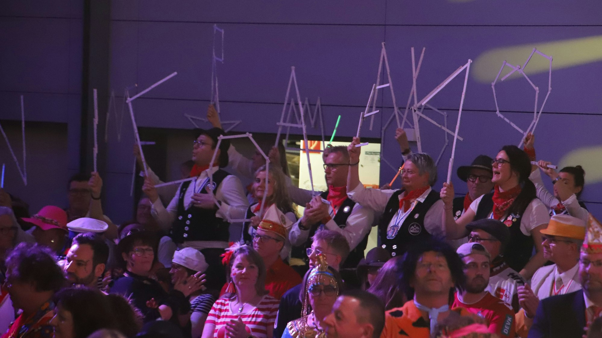 Besucher einer Karnevalssitzung formten aus Zollstöcken Buchstaben.