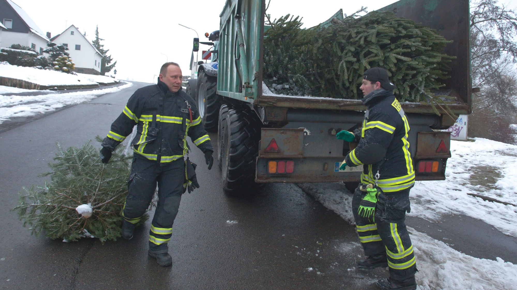 Das Foto zeigt zwei Feuerwehrmänner, die ausgediente Weinachtsbäume auf einen Anhänger laden.