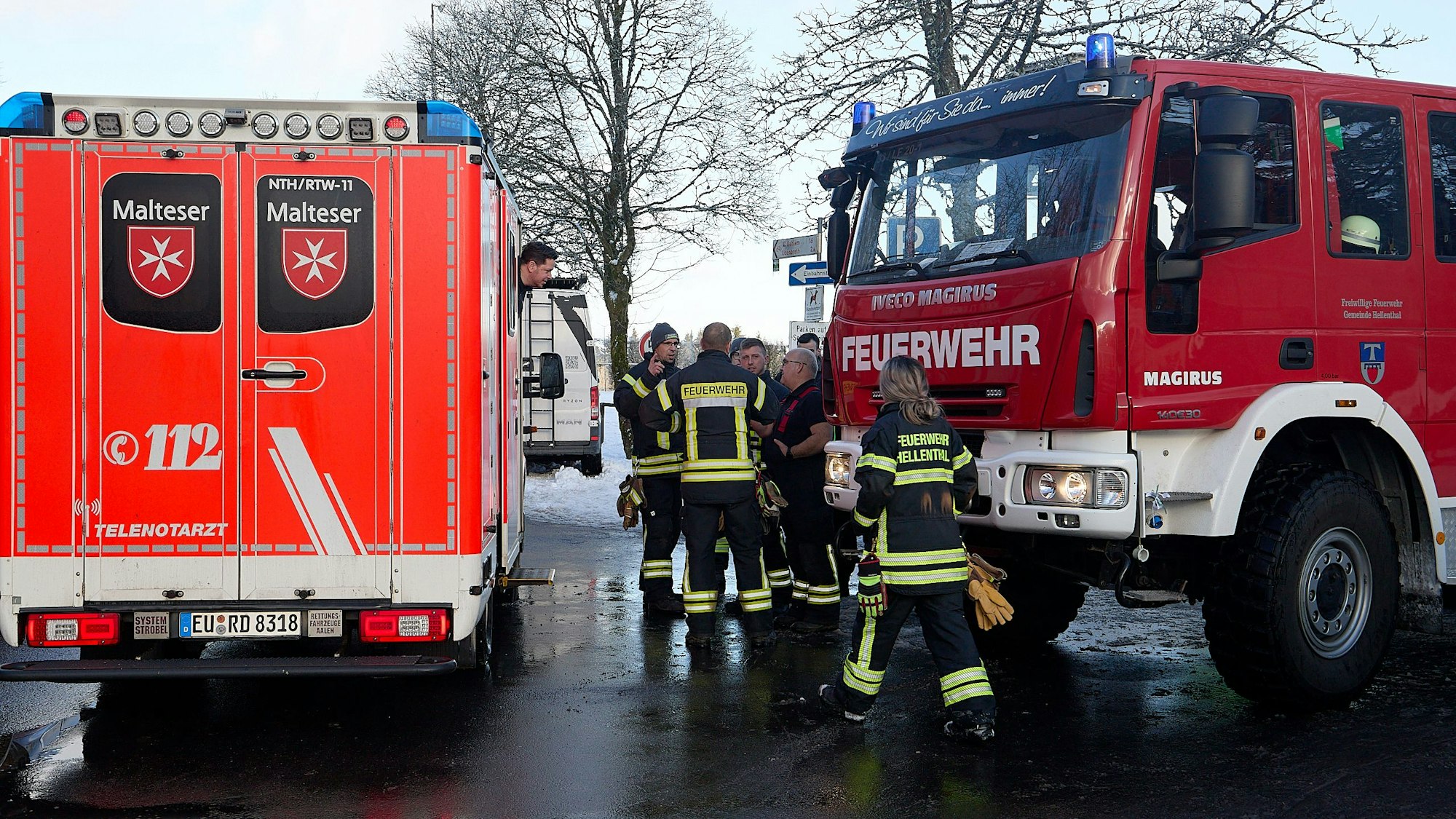 Ein Feuerwehrfahrzeug und ein Rettungswagen stehen am Weißen Stein in Udenbreth. Einige Feuerwehrleute in Einsatzkleidung stehen daneben.