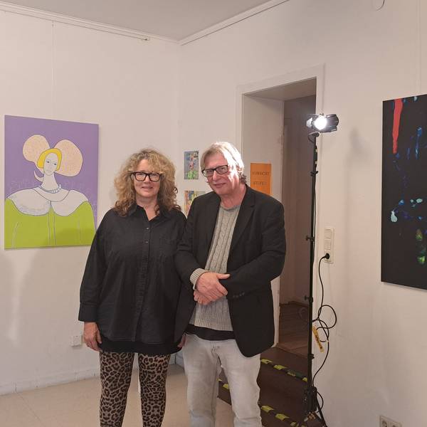 Eine Frau und ein Mann stehen zwischen Kunstwerken, die links und rechts von ihnen an der Wand hängen.