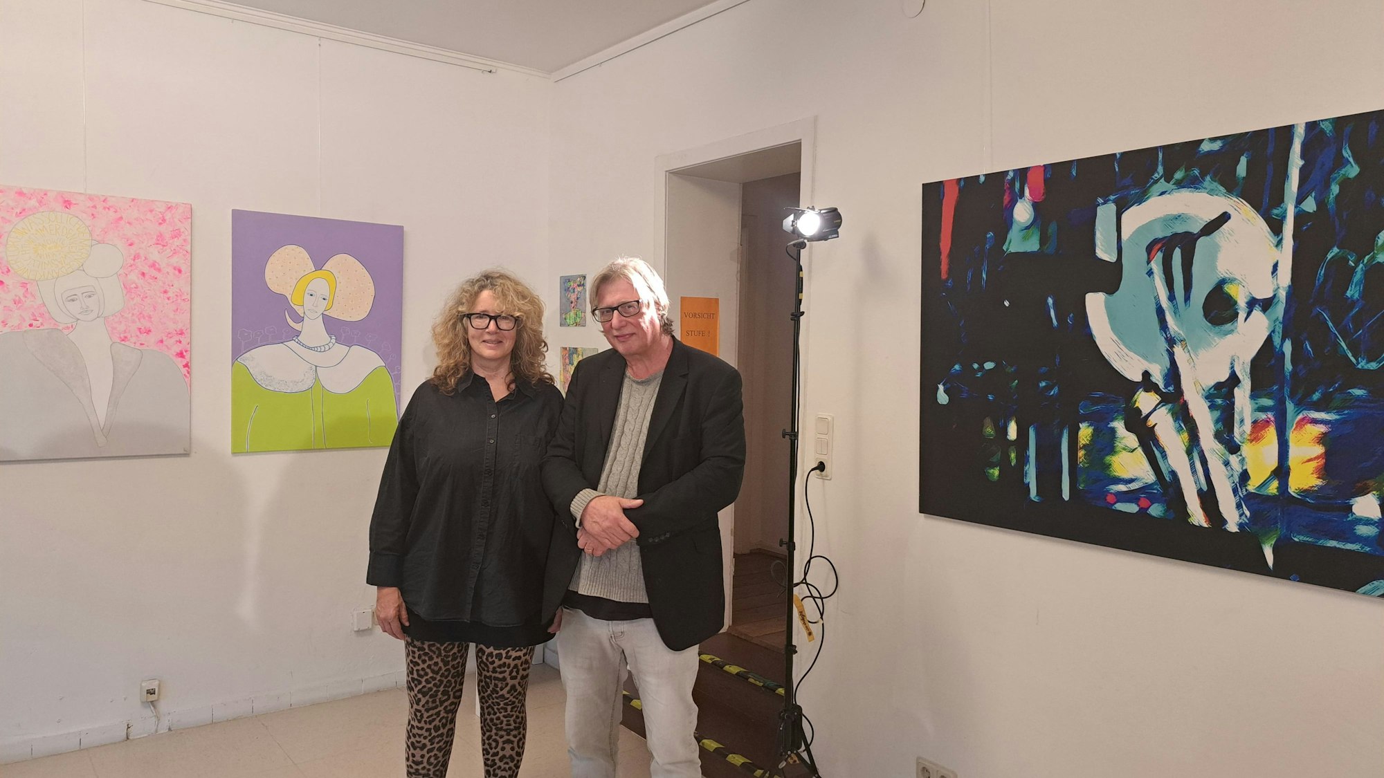 Eine Frau und ein Mann stehen zwischen Kunstwerken, die links und rechts von ihnen an der Wand hängen.