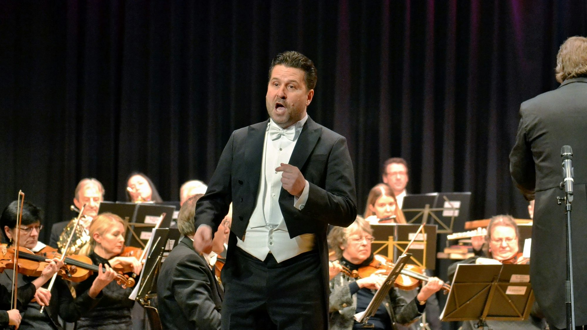 Das Foto zeigt den Solisten Daniel Szeili. Im Hintergrund ist das Orchester zu sehen.