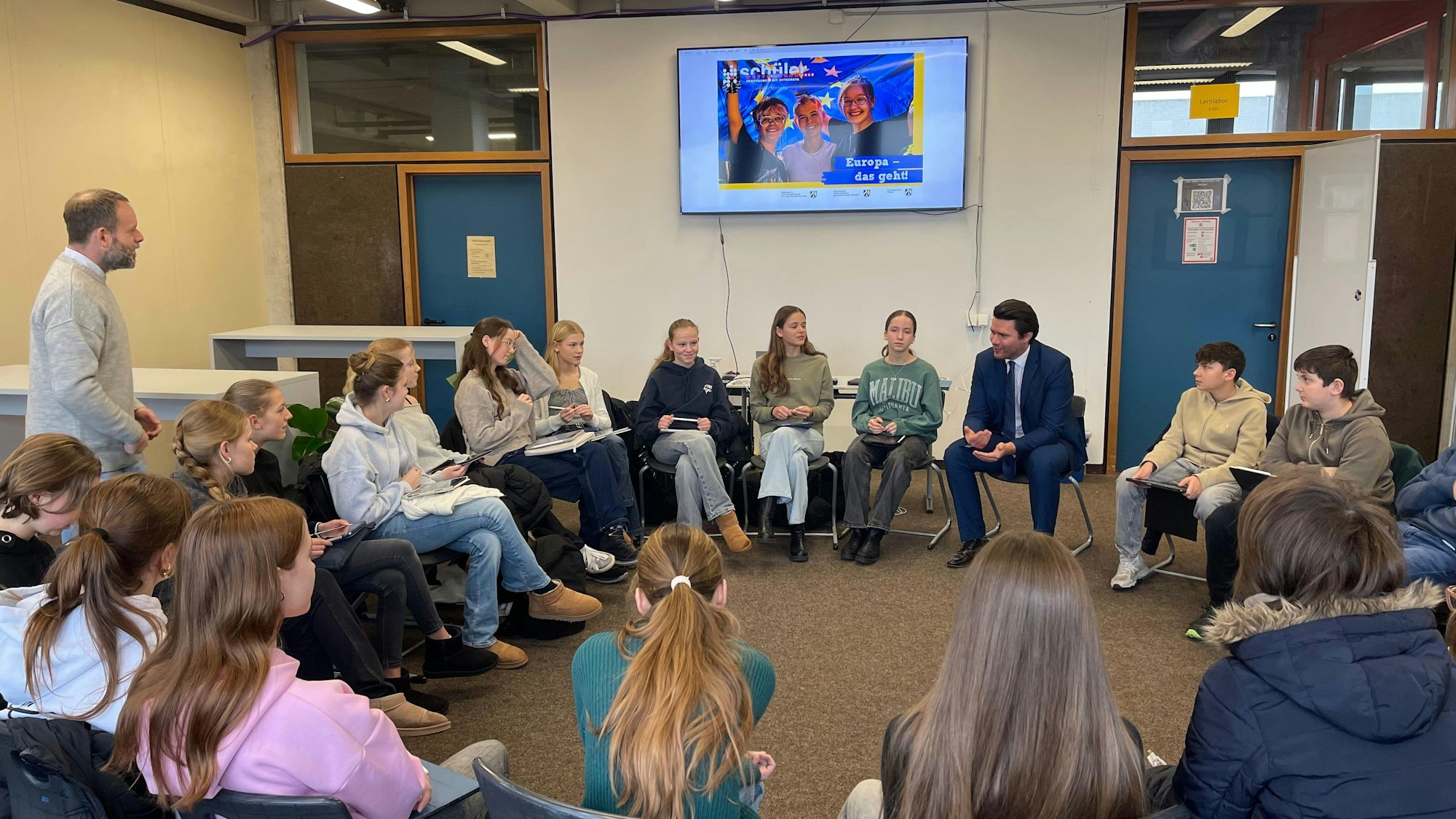 Das Foto zeigt eine Schulklasse im Stuhlkreis mit dem CDU-Politiker Thomas Okos.