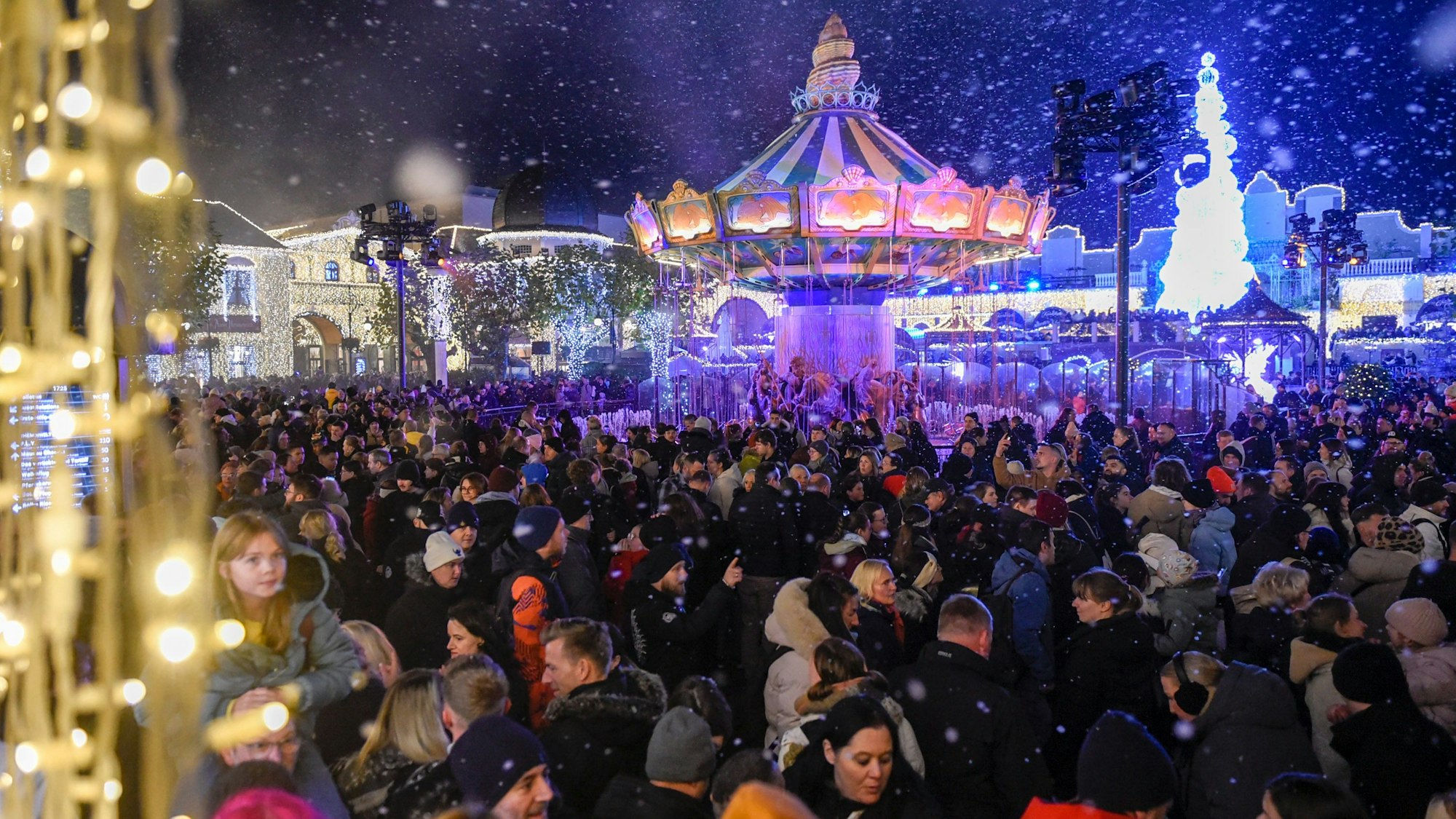 Zahlreiche Menschen stehen in einem Freizeitpark vor einem großen Karussell.