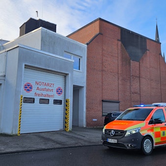 Zu sehen ist das Krankenhaus in Bedburg, im Vordergrund das Fahrzeug des Notarztes im Einsatz mit Blaulicht.