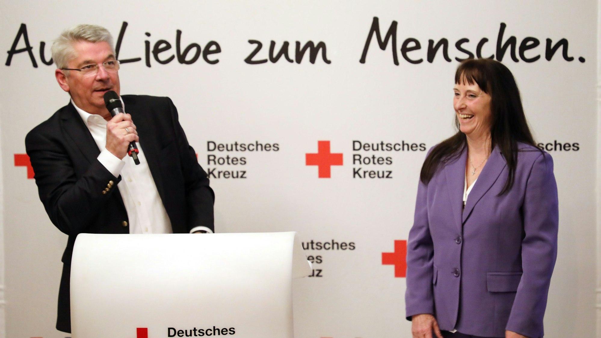 Ingeborg Schmidt und ihr Nachfolger im DRK-Kreisvorsitz Lutz Urbach stehen vor einer DRK-Wand an einem Rednerpult.