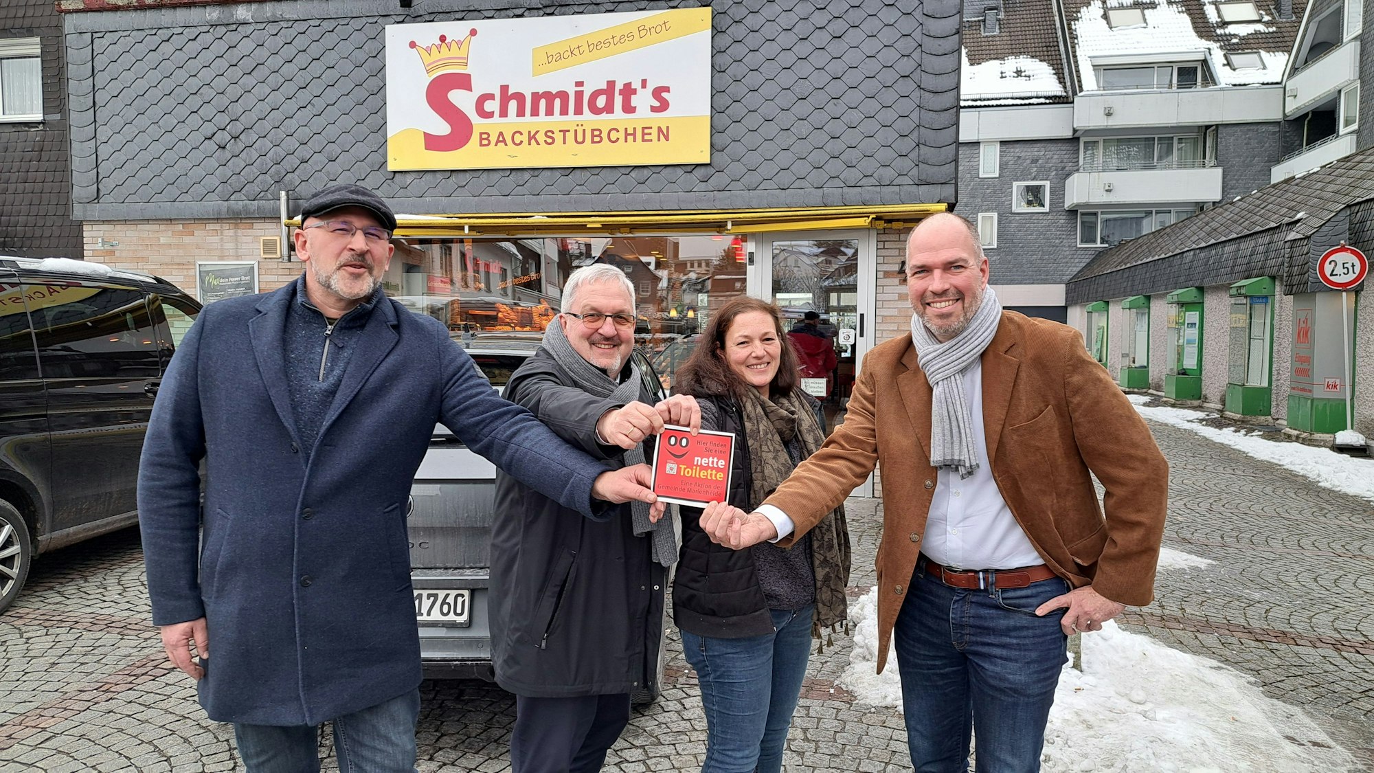 Mehrere Männer halten gemeinsam ein rotes Hinweisschild in den Händen mit der Aufschrift „Nette Toilette“.