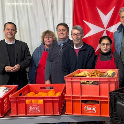 Menschen stehen hinter einem Tisch, auf dem Lebensmittel stehen.