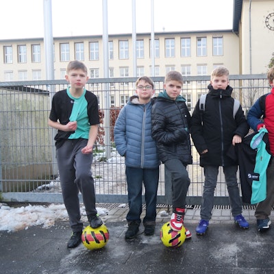 Sechs Jungs stehen vor einem verschlossenen Schulhof-Tor.