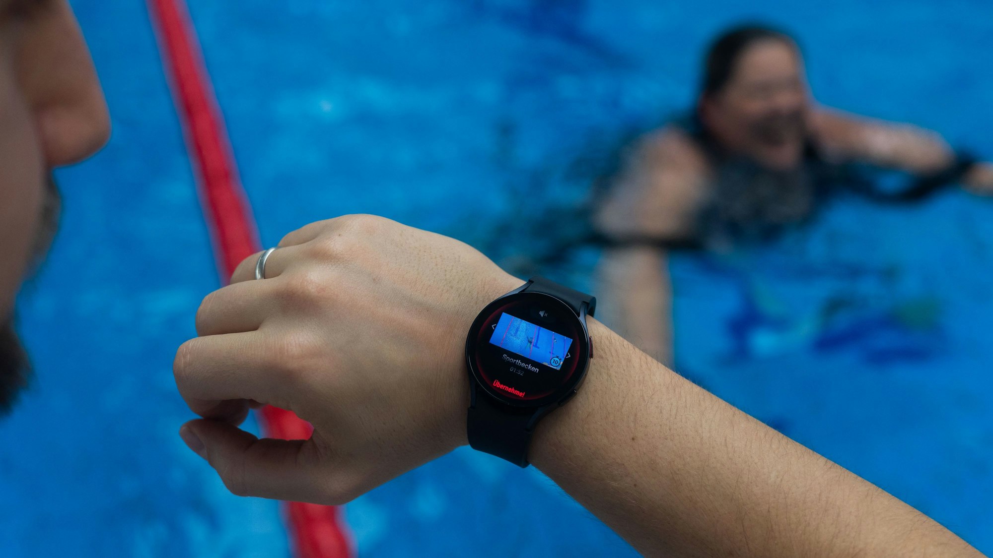 Ein Bademeister trägt eine Smartwatch am Handgelenk, die ein Warnsignal zeigt.