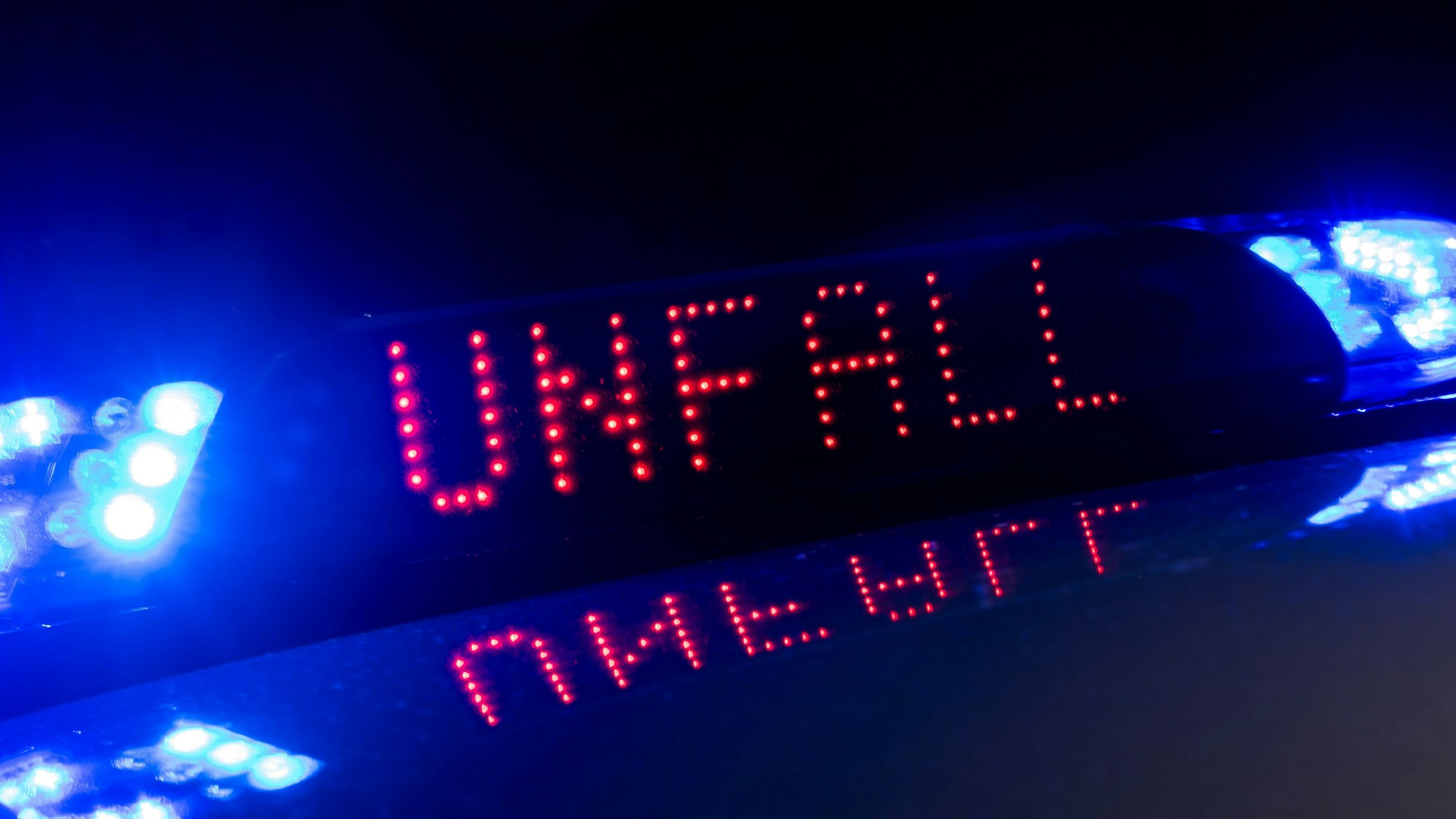 Das Blaulicht auf einem Fahrzeug der Polizei leuchtet in der Dunkelheit, während auf dem Display der Hinweis „Unfall“ zu lesen ist.