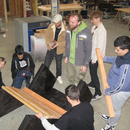 Jugendliche und Erwachsene mit Hölzern in einer Schreinerei.