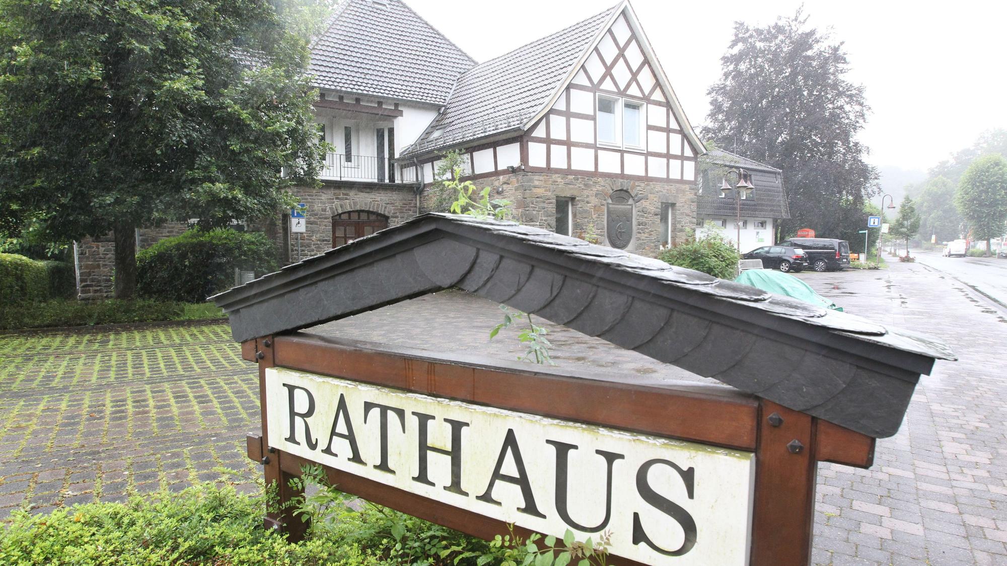 Ein Schild mit der Aufschrift „Rathaus“ vor einer Einfahrt und einem Gebäude mit Bruchsteinmauern und Fachwerk.