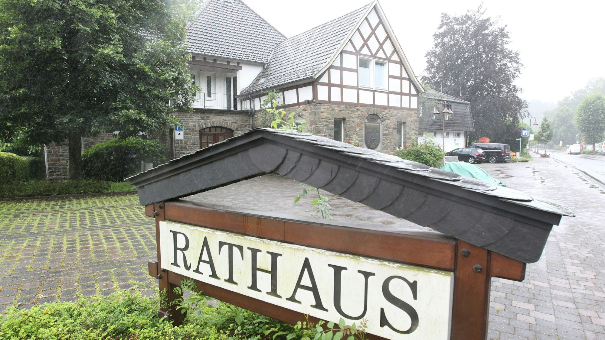 Ein Schild mit der Aufschrift „Rathaus“ vor einer Einfahrt und einem Gebäude mit Bruchsteinmauern und Fachwerk.