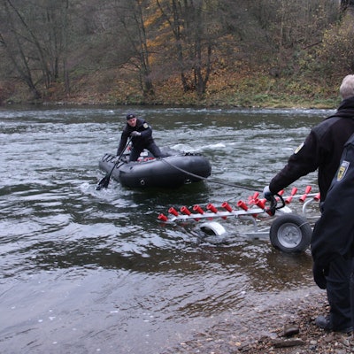 Ein Polizist steht in einem Boot, das noch auf dem Wasser schwimmt, ein Anhänger und zwei weitere Polizisten stehen bereit.