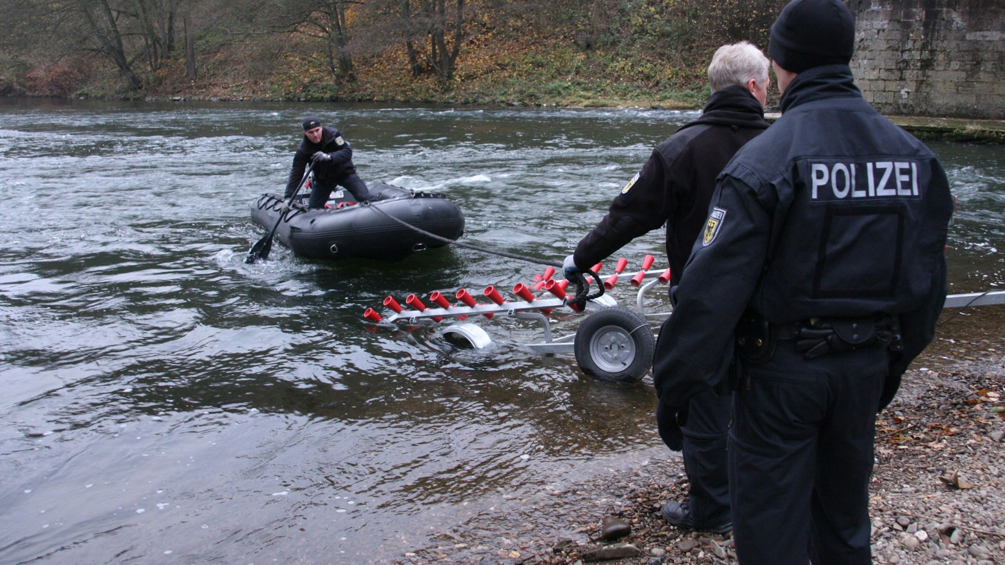 Ein Polizist steht in einem Boot, das noch auf dem Wasser schwimmt, ein Anhänger und zwei weitere Polizisten stehen bereit.