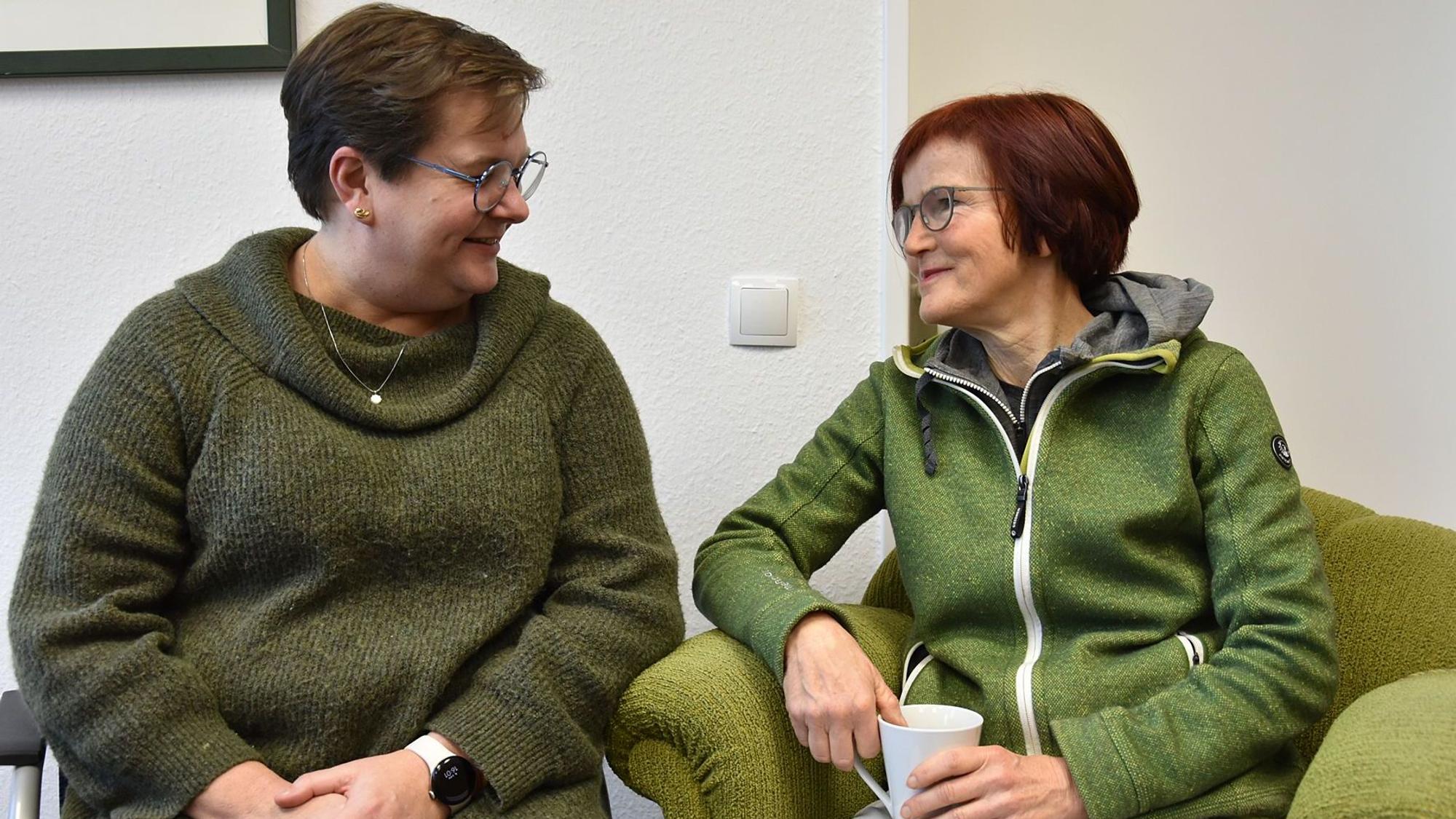 Zwei sitzende Frauen blicken sich freundlich an.