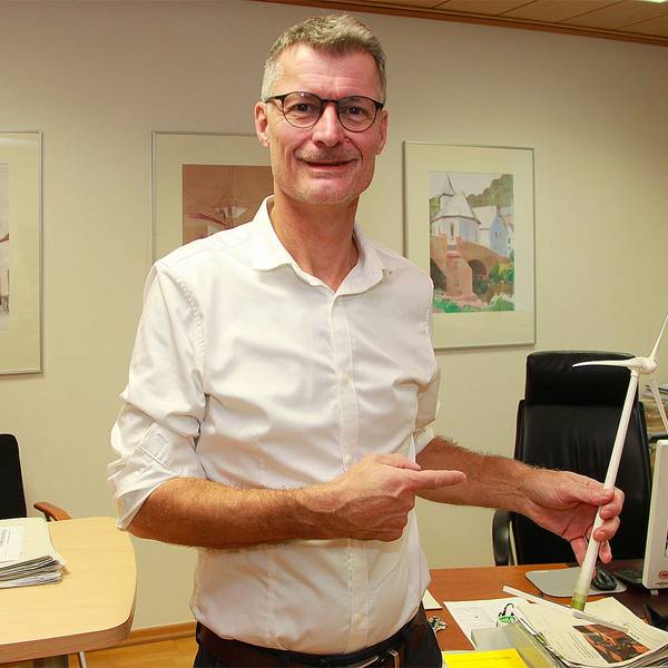 Das Bild zeigt Jan Lembach in seinem Büro. Er hält das Modell einer Windkraftanlage in der Hand.