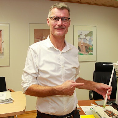 Das Bild zeigt Jan Lembach in seinem Büro. Er hält das Modell einer Windkraftanlage in der Hand.